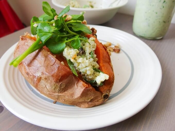 A large baked sweet potato on a ceramic plate, cut in half and stuffed with green quinoa and topped with chopped watercress.