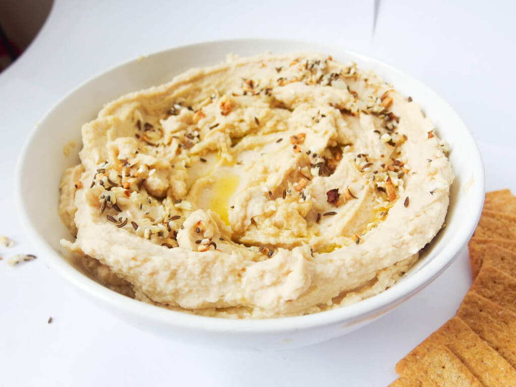 close up of everything hummus swirled served in a white bowl