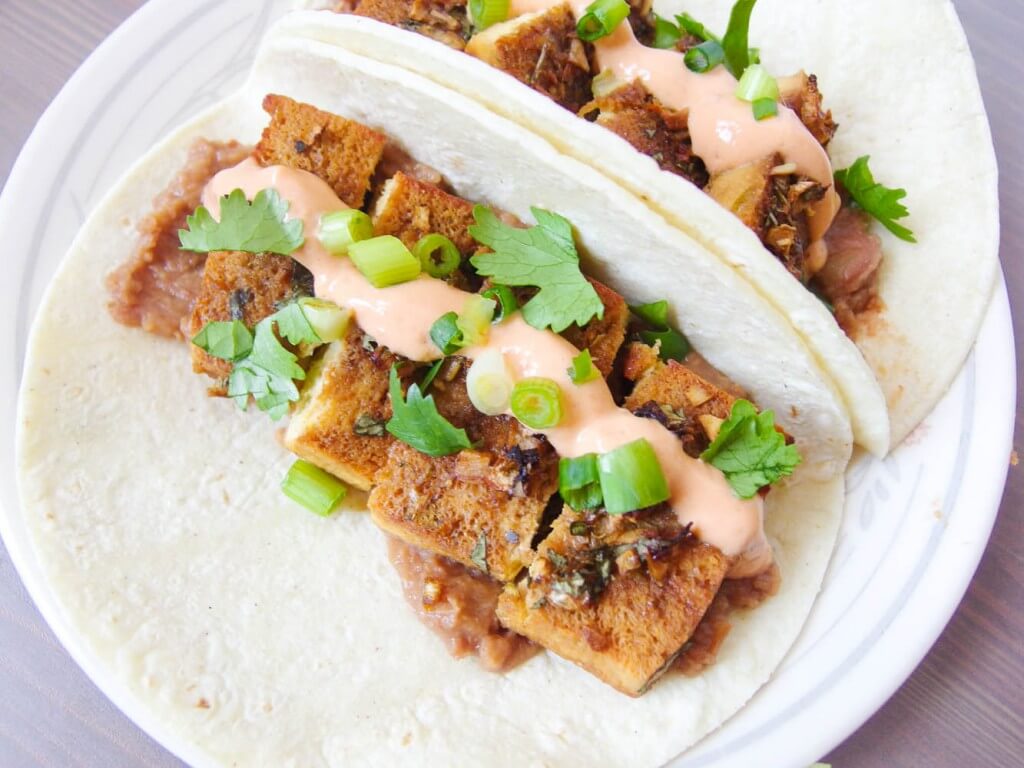 close up of two tequila lime tofu tacos with chipotle crema served with scallions and onion
