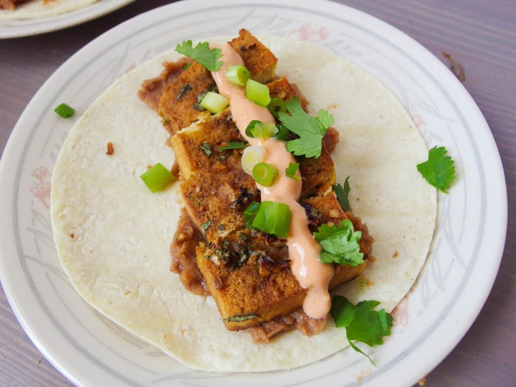 tequila lime baked tofu taco open face served with chipotle crema, cilantro, and scallions on a white plate