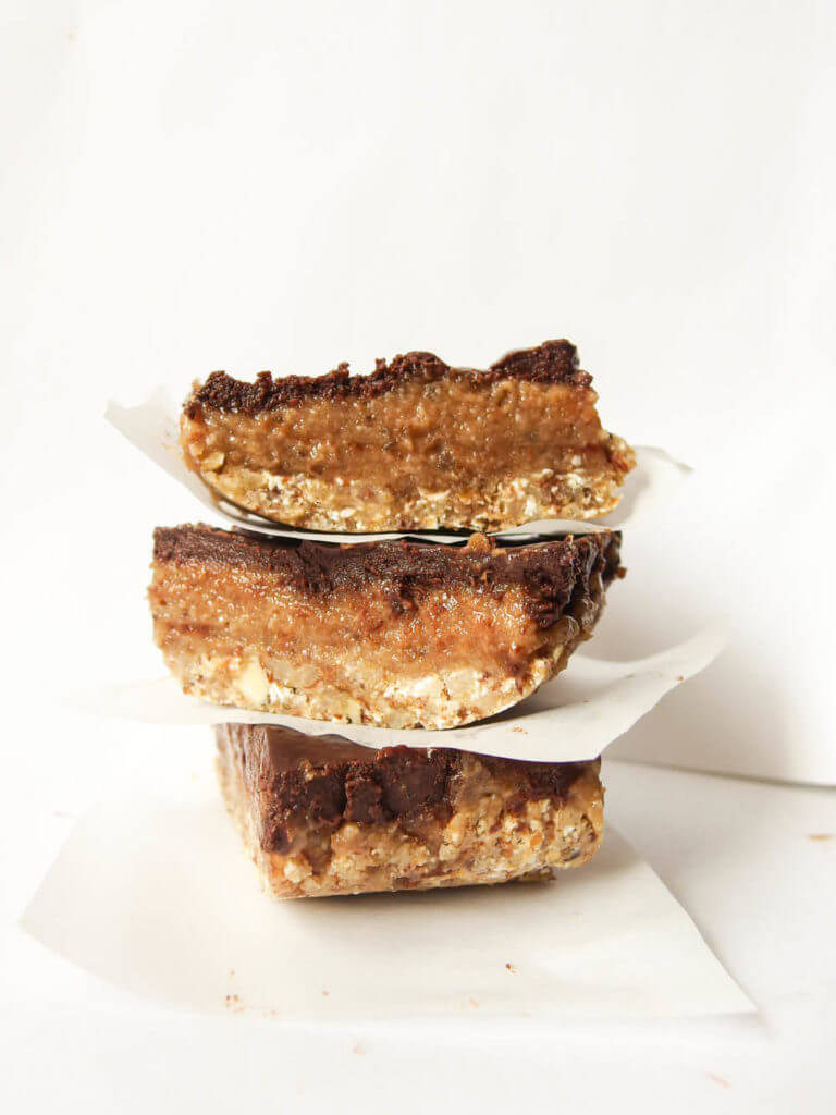 Close-up of Three Vegan Gooey Date Caramel Mocha Bars stacked with parchment paper and espresso topping