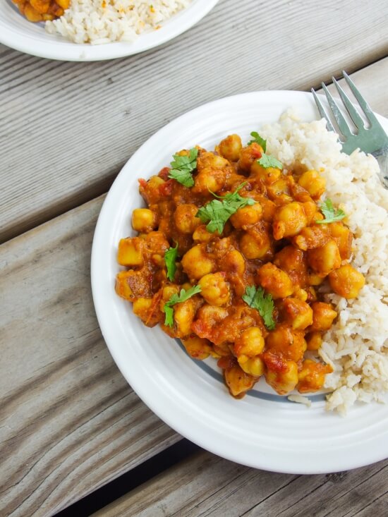 Vegan spicy chickpea curry with fresh ground spices garnished with cilantro served with fluffy rice on a white plate