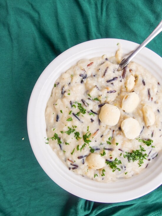 Overhead view of creamy vegan wild rice soup in a bowl, garnished with oyster crackers and chopped parsley.