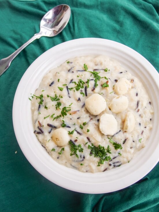 Vegan wild rice soup in a white bowl on a teal background with a metal spoon