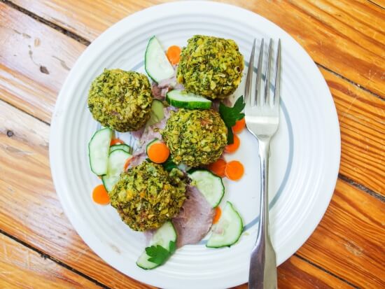 Four easy baked crispy and crumbly Kale Falafel servied on a white plate with carrots, cucumber, and cilantro | yupitsvegan.com