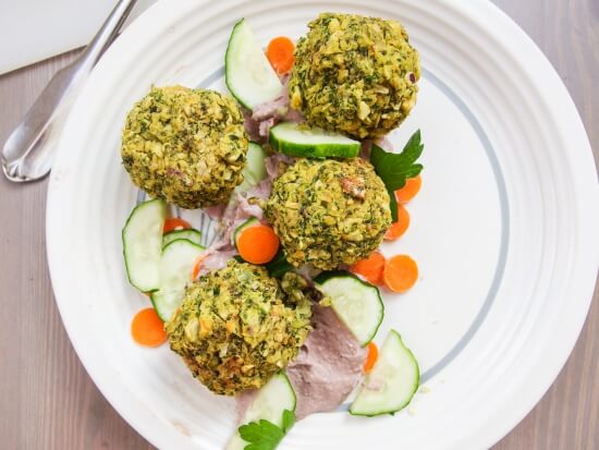 Closeup of four fresh homemade oil free baked kale falafel with onion, garlic, and lemon garnished with parsley and cilantro and served with creamy smooth hummus - nutritious option for comfort food