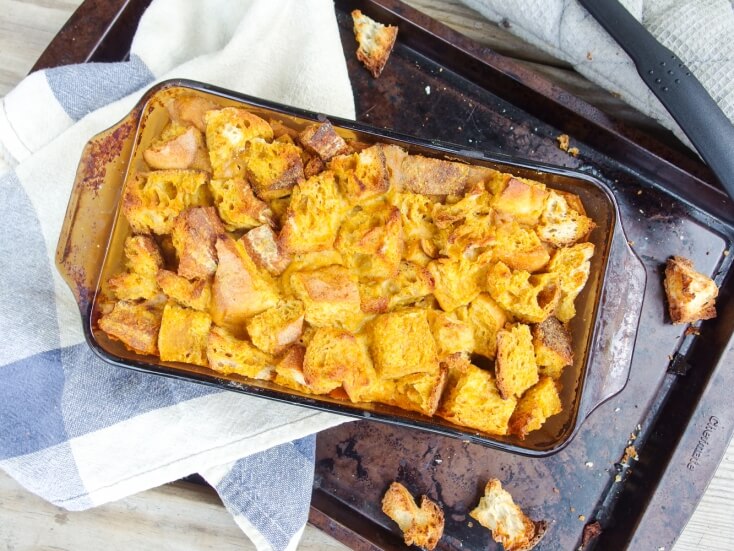 Decadent vegan pumpkin bread pudding - egg free and dairy free - with sweet maple syrup and rum served in a baking pan over a blue checked towel