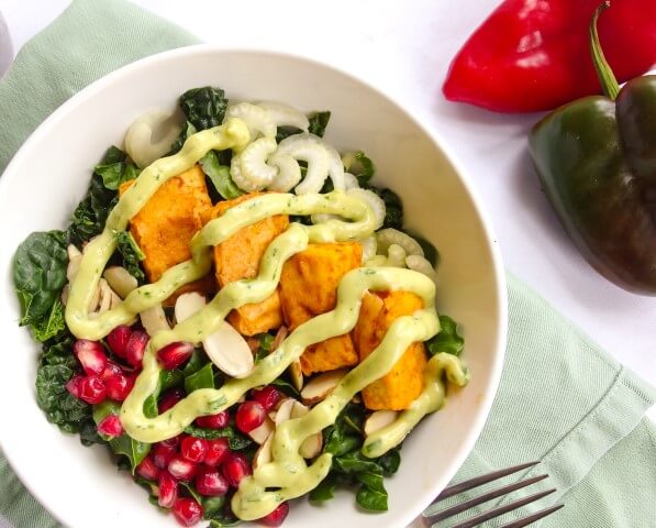 Closeup of a hearty, nutrient dense lacinato kale salad with fresh crisp red bell pepper, spicy baked buffalo tofu, sweet pomegranate arils, and a creamy ranch avocado ranch dressing 