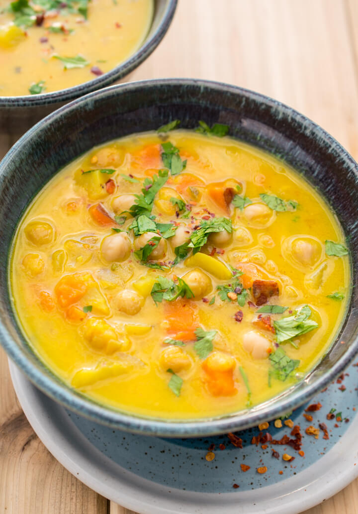 Close-up of a bowl of turmeric chickpea stew, showing the vibrant yellow color, and chunks of sweet potato, chickpea, and fresh cilantro.