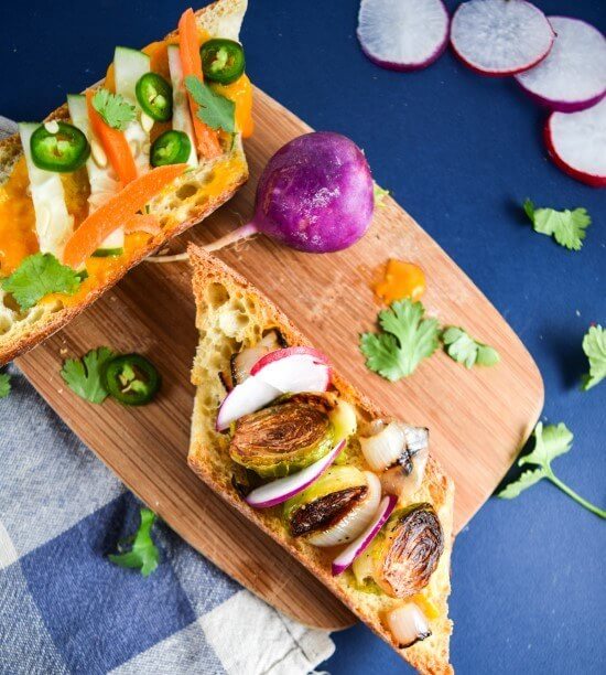 Vegan banh mi sandwiches stuffed with crispy roasted Brussels sprouts, a simple mango sriracha sauce, and tons of fresh veggies served on a cutting board with crispy radish slices | yupitsvegan.com