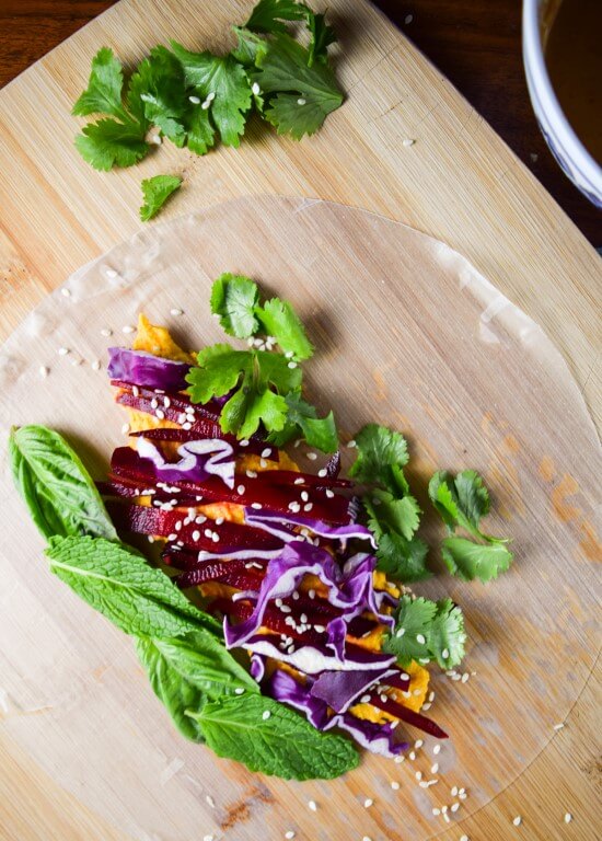 Close up of one unwrapped spring roll laid out prepared. Fresh green herbs, crunchy cabbage, and smooth beets topped with sesame seeds