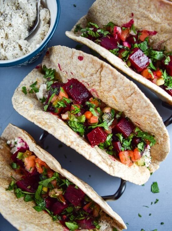 Three tacos with spicy chipotle roasted beets, fresh chunky pico de gallo salsa, creamy vegan from scratch cashew queso, and bright cilantro in tortillas