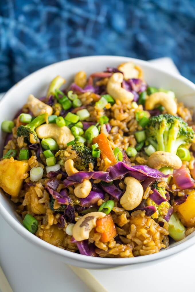 Close up of sweet and spicy homemade stir fry sauce with fluffy brown fried rice, toasted nuts, healthy veggies, and tart pineapple for a healthy glutenfree lunch bowl