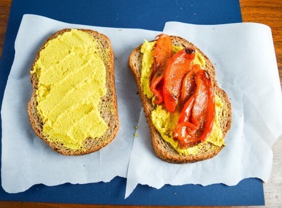 Open face sandwich in assembly with from scratch mango curry hummus and tandoori spice rubbed slow roasted sweet red peppers on whole grain bread