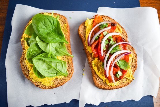 Open face sandwich with all the fixings. Leafy green spinach, spicy red onion, cilantro, flavorful roasted red bell peppers, and homemade sweet mango curry hummus on panini bread