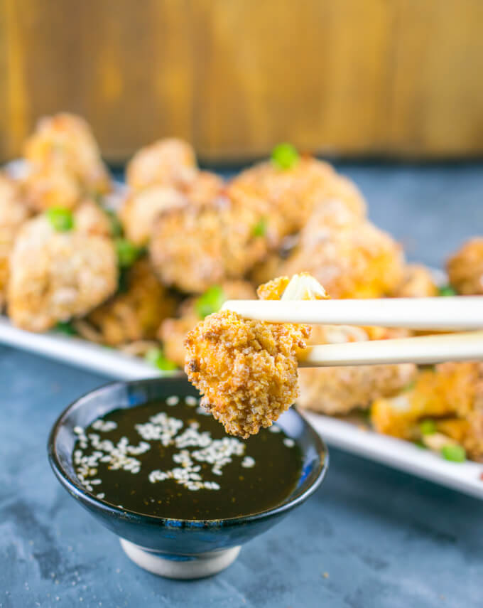 A single Thai peanut cauliflower wing being dipped into a small ceramic bowl of dipping sauce with chopsticks.