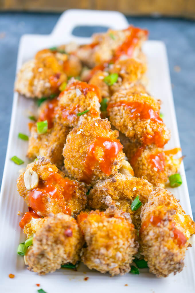 A full tray of Thai peanut cauliflower wings, drizzled with sriracha sauce and garnished with chopped scallions.