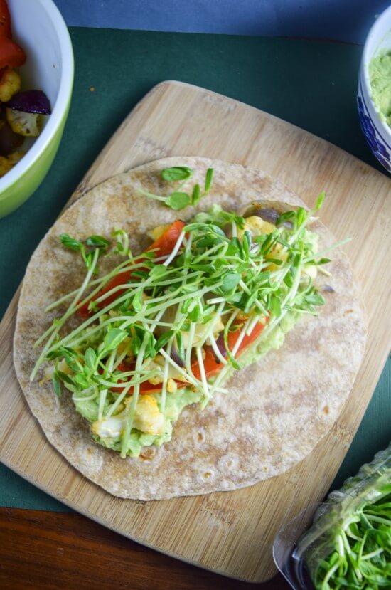 Skillet warmed wrap bread with smooth mashed avocado, coconut sugar sweetened roasted vegetables, and fresh sprouts