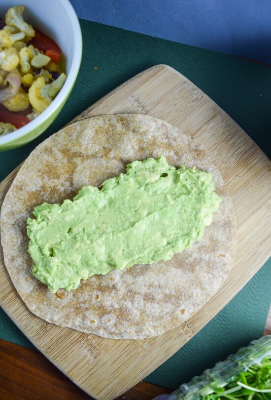 Warm whole grain tortilla with creamy avocado mash prepared for roasted vegetables - perfect nut free vegan lunch or dinner 