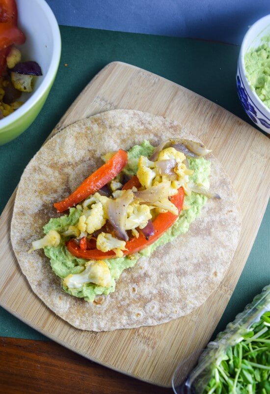 Hot whole wheat tortilla wrap with rich mashed avocado, hearty roasted red bell pepper, cauliflower, and red onion, garnished with black pepper and salt - delicious soy free vegetarian meal!