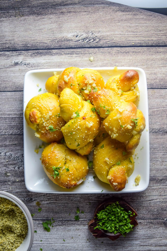 A plate of soy free and nut free vegan pumpkin garlic knots infused with intense garlic flavor and olive oil and topped with fresh nut cheese and parsley