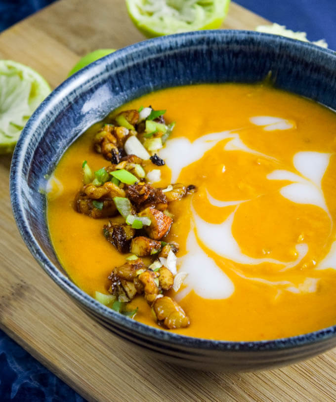A blue bowl of thai roasted butternut squash soup made with coconut milk, caramelized squash puree, thai red curry paste garnished with toasted almonds and walnuts in tamari and sriracha | Yup, it's Vegan