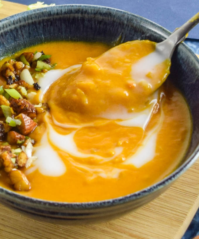 Close up of a spoonful of creamy sweet and spicy thai inspired butternut squash soup with toasted savory nuts