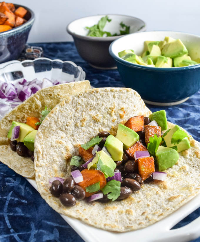 Barbecue sweet potato tacos with spiced black beans, creamy avocado, and spicy red onions garnished with cilantro