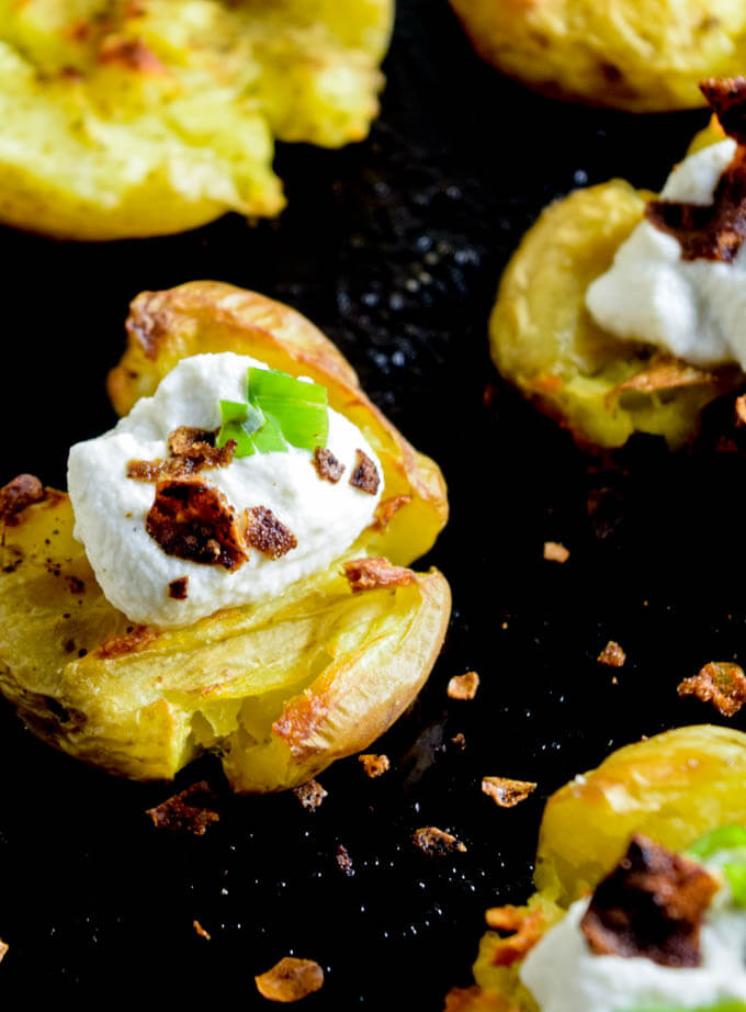 Closeup of loaded baked potato with fluffy inside and crunchy potato skin, topped with decadent nut cream and savory homemade rice paper bacon, and fresh herbs | yupitsvegan.com