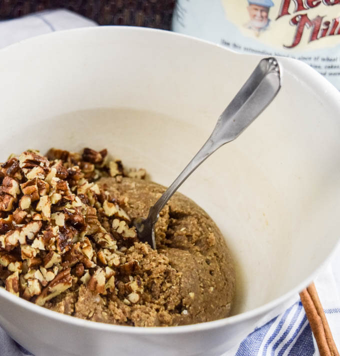 White bowl of ingredients for gluten-free and vegan maple pecan cookies - fresh toasted pecans folding into a perfectly soft and edible dough