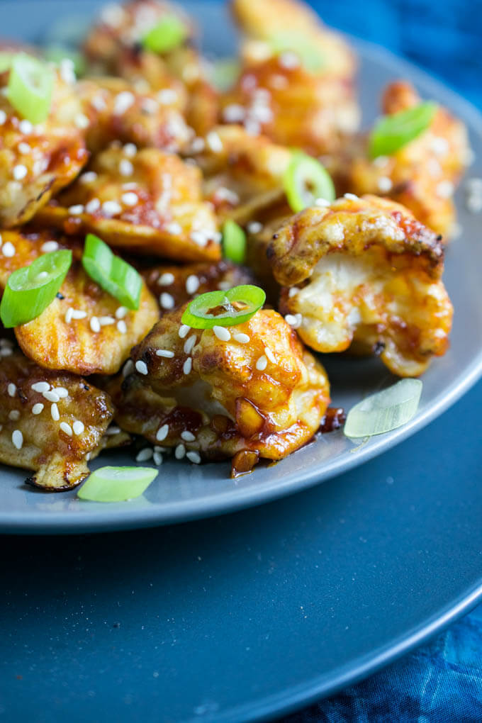 Closeup of gluten free asian inspired baked cauliflower coated in a homemade sticky sesame sauce featuring garlic, ginger, agave, and sriracha, garnished with green onions and sesame seeds