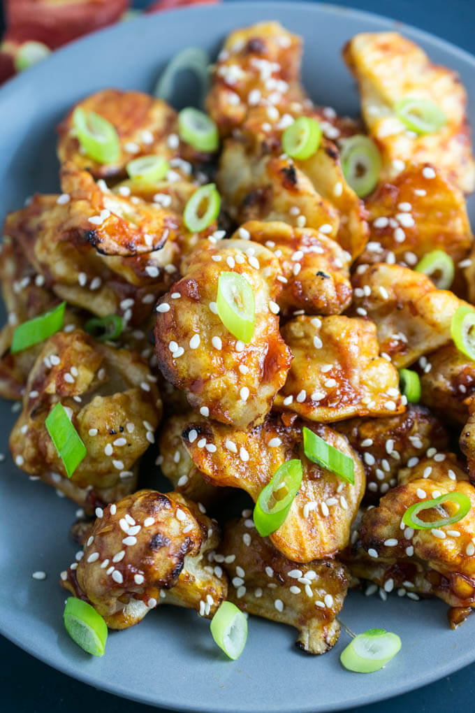 Close up of healthy vegan appetizer - light and tender baked cauliflower bites with homemade sweet and spicy sesame sauce topped with green onions and crunchy seeds