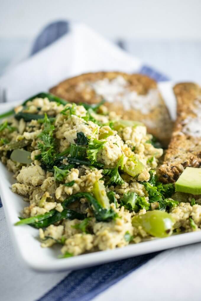Green tofu scramble on a white plate with a blue and white striped napkin and gray background.