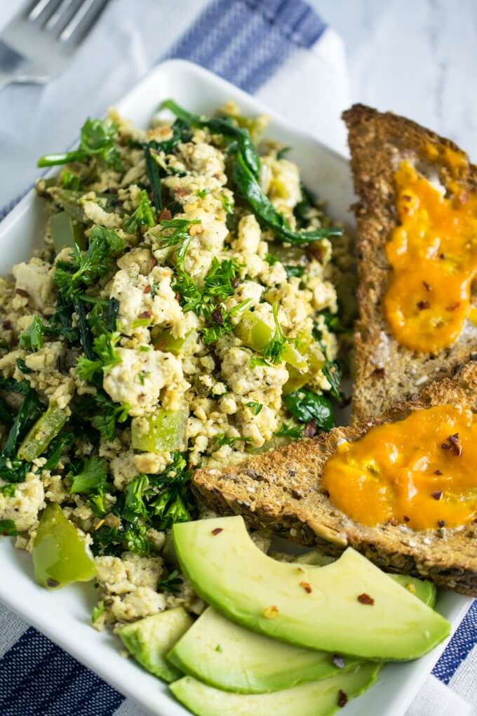 Overhead view of tofu scramble on a plate with vegan buttered toast, avocado, and chili flakes for garnish.