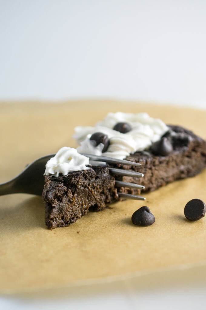 Close up of a forkful of decadent fudgy chocolate cake with no flour and secret healthy ingredients - sweetened with brown rice syrup to be refined sugar-free and garnished with vegan whipped cream and chocolate chips