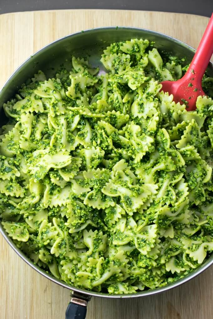 Bowtie pasta tossed with bright green edamame pesto in a steel skillet on a wooden cutting board