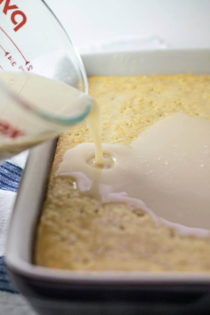 Sweetened condensed coconut-macadamia milk is poured over a baked vegan sponge cake with holes poked in it.