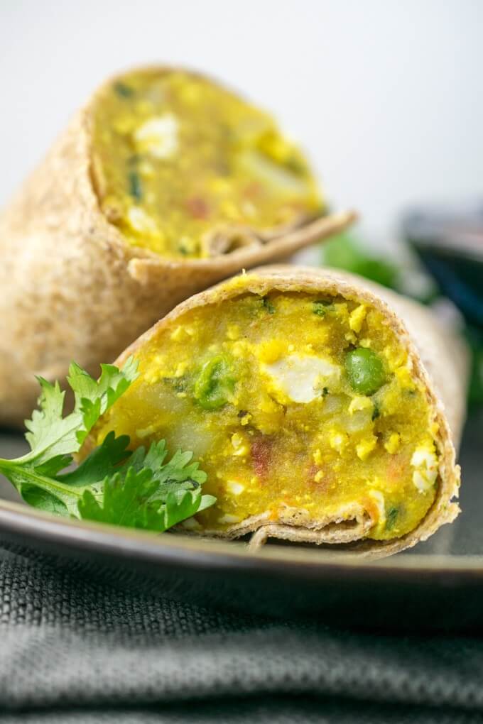 Spiced mashed potatoes, peas, and tomatoes wrapped in a brown tortilla with fresh coriander and a second wrap in the background.