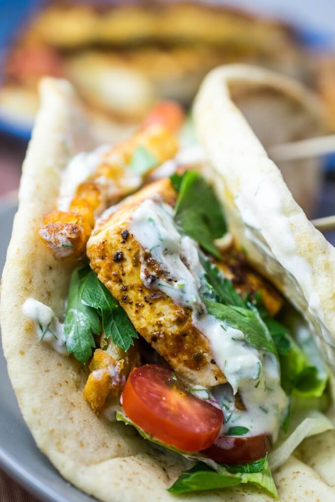 Closeup of folded pita bread filled with browned tofu, cherry tomato, parsley, yogurt sauce, and French fries.