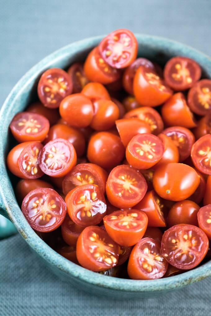 Sliced fresh cherry tomatoes in a blue ceramic bowl on a gray linen napkin, ready to be used in burst cherry tomato sauce.