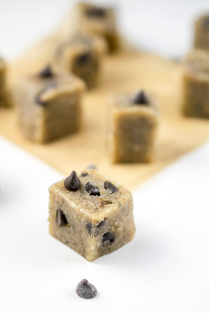 Vegan chocolate chip cookie dough squares arranged on parchment paper with additional chocolate chips on top for garnish.
