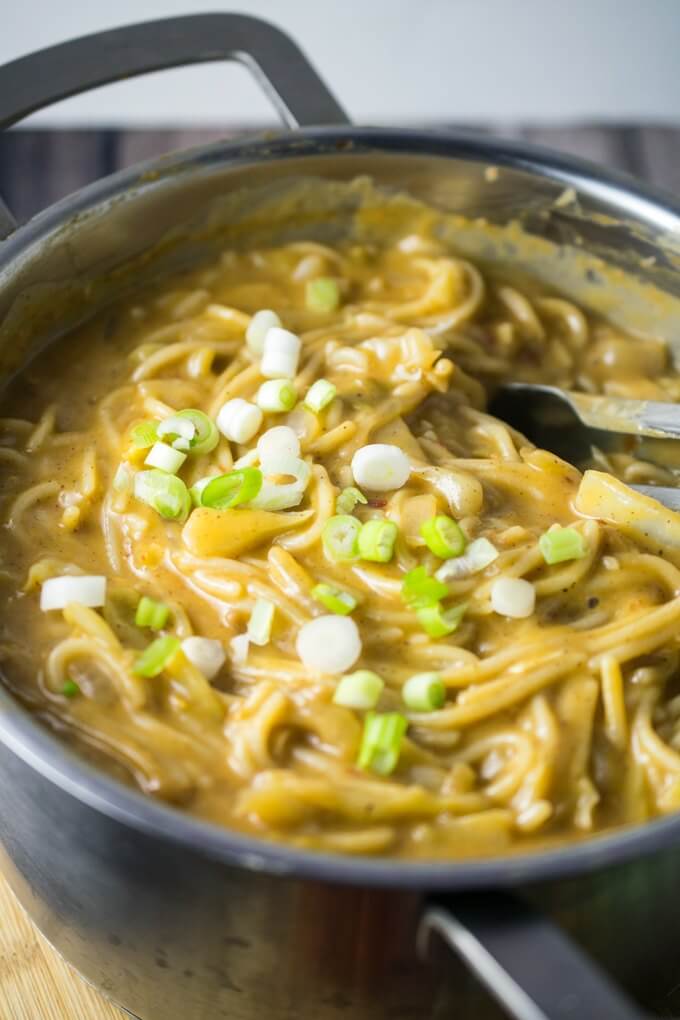 Un pentolone pieno di cremosi noodles al burro di mandorle, mescolati con le pinze e guarniti con scalogni tritati.