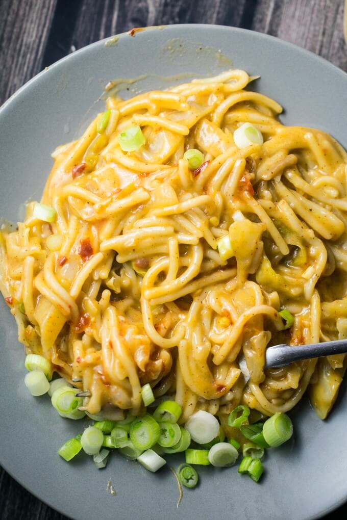 A heaping plateful of creamy almond butter noodles, garnished with scallions and chili flakes, on a gray plate and wooden table.