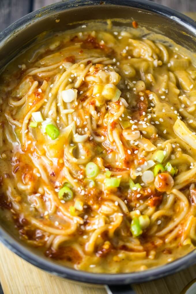 One Pot Chili Garlic Almond Butter Noodles într-o tigaie cu sos de ardei iute și usturoi stropit deasupra, presărat cu ceapă verde și semințe de susan.