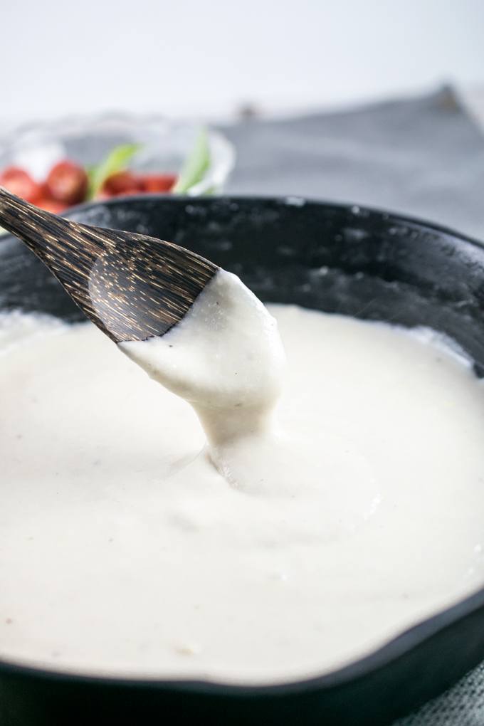 Vegan mozzarella in a cast iron skillet, being stirred with a wooden spoon.