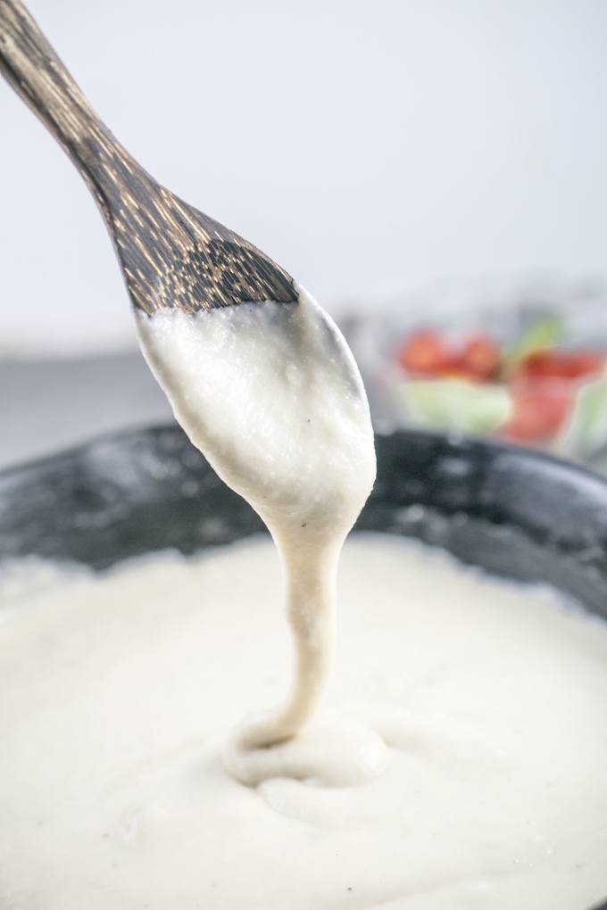 Vegan mozzarella being drizzled from a wooden spoon into a pan, stretching as it falls.