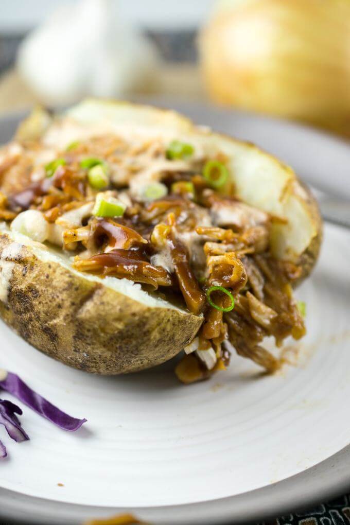 Close-up of a BBQ jackfruit stuffed baked potato garnished with cashew cream sriracha aioli and chopped green onions