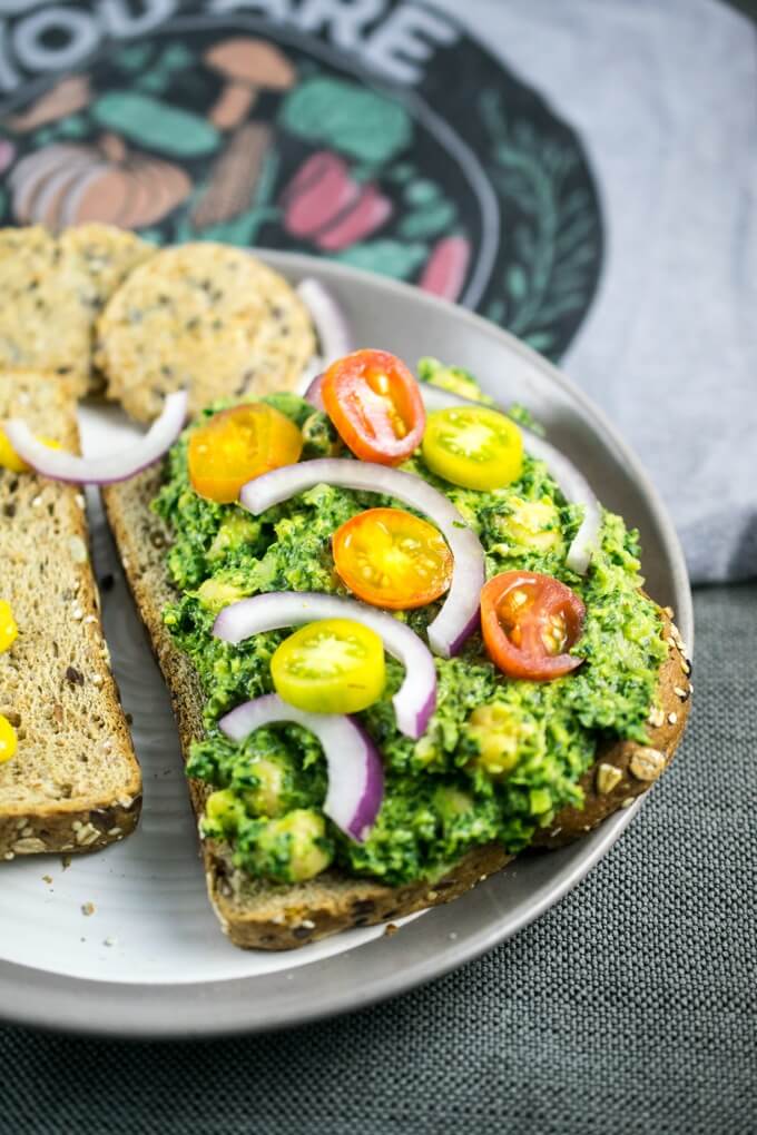 Collard green chickpea pesto smashed sandwiches with onion, mustard, tomato, Mary's Gone Crackers, on a gray and white plate.