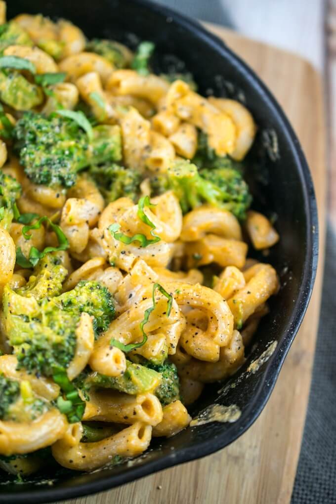 Close-up of macaroni noodles coated with potato and carrot-based vegan cheese sauce, with basil chiffonade basil and blanched broccoli