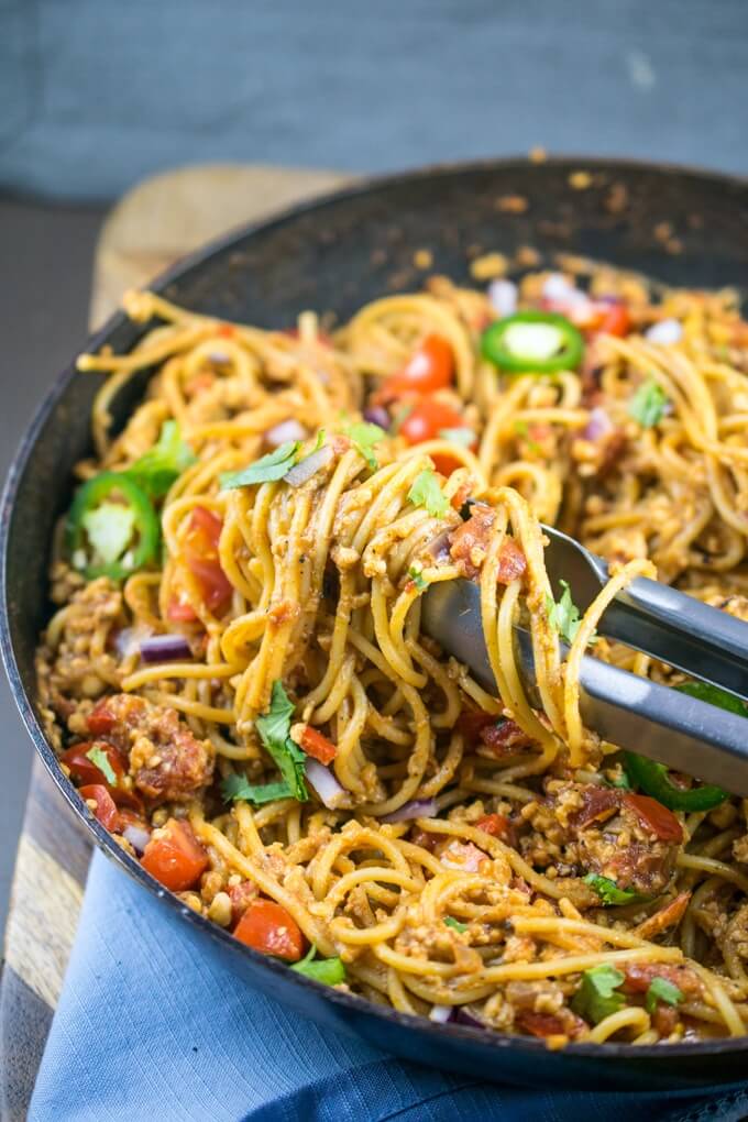 One pot taco spaghetti being twirled with a pair of tongs, with fresh coriander and tomato on top and a gray napkin in the background.